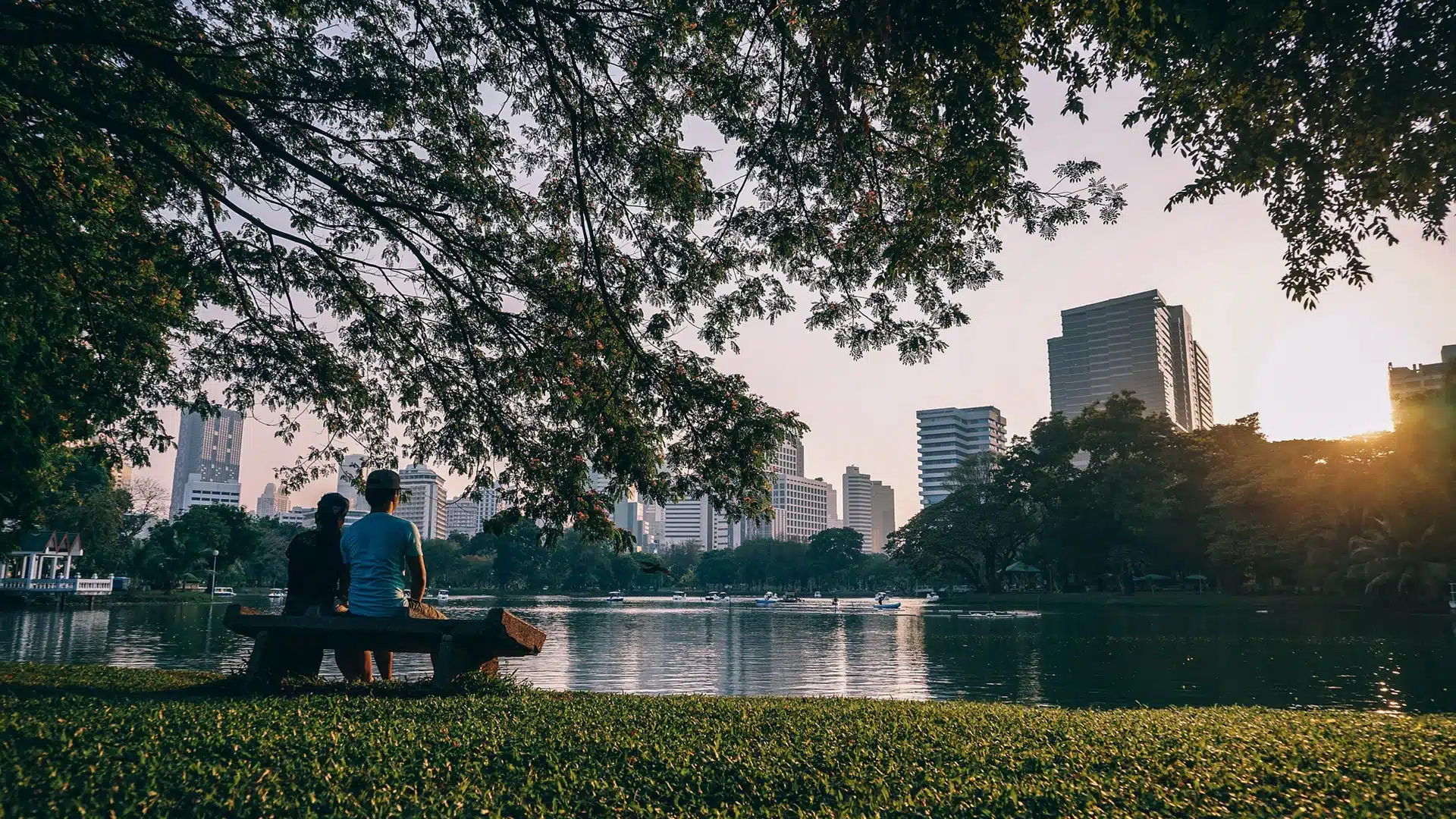 Δύο άνθρωποι που κάθονται σε ένα παγκάκι μπορστά σε μία λίμνη σε ένα πάρκο με θέα τους ουρανοξύστες
